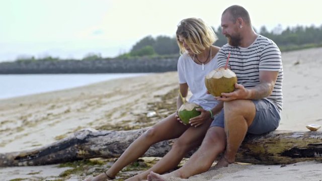 Romantic couple talking and drinking coconut cocktails while sitting on sandy ocean beach