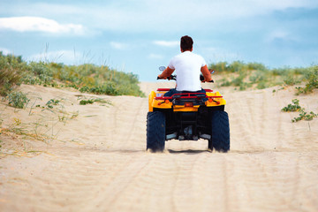 rear view of man riding atv quad bike at sandy beach, summer vacation sport