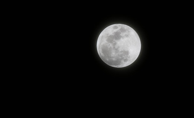 Full moon shines bright against dark black night sky