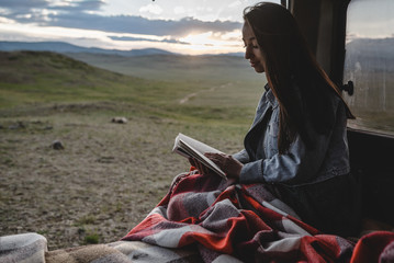 two young girls sitting in the van and reading a book. beautiful sunset in mountain valley on the background. - 212743945