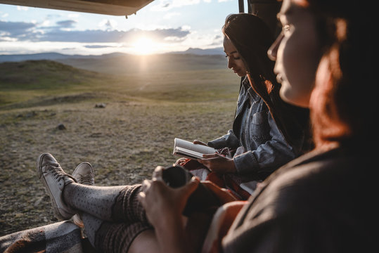 two young girls sitting in the van and reading a book. beautiful sunset in mountain valley on the background.
