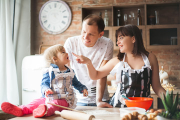 Cute little girl and her beautiful parents are smiling while cooking in kitchen at home