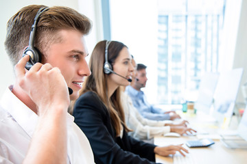 Smiling friendly man working in call center office with team