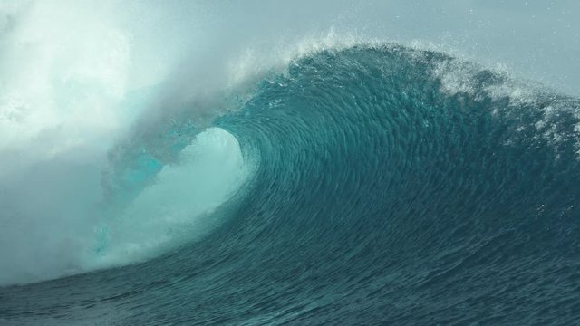 SLOW MOTION, CLOSE UP: Glimmering barrel wave rushes past the camera on a sunny day in Tahiti. Big tube wave sprays sparkling drops of ocean water high in air while it approaches a remote island.