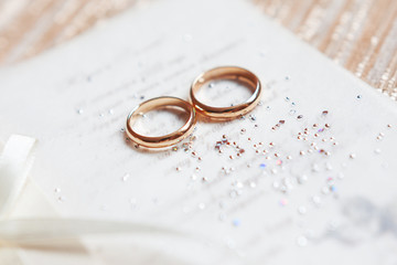 Golden wedding rings on paper invitation with shiny rhinestones. Wedding details, symbol of love...