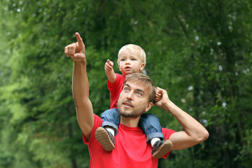 Cute toddler boy sits on his father's shoulders. They point fingers in the same direction....