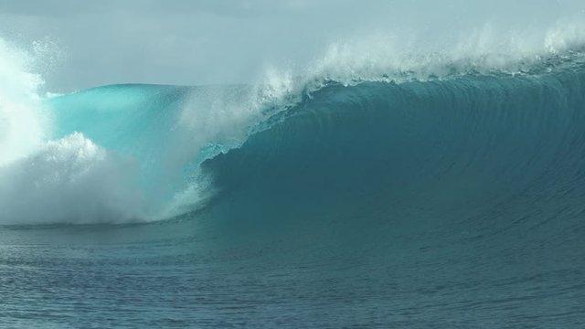 SLOW MOTION, CLOSE UP: Foaming ocean water splashes high in the sky near a big barrel wave breaking towards French Polynesia. Large emerald tube wave shining in the summer sun curls and crashes wildly