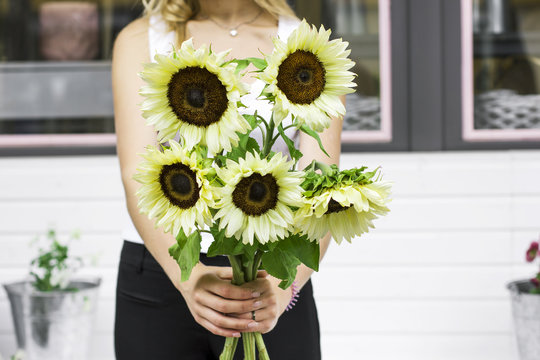 Young woman holding decorative light yellow sunflowers in the street near flower shop