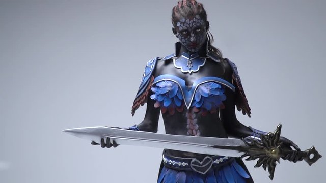 A dark elf woman in a feather armor holds a sword in her hands