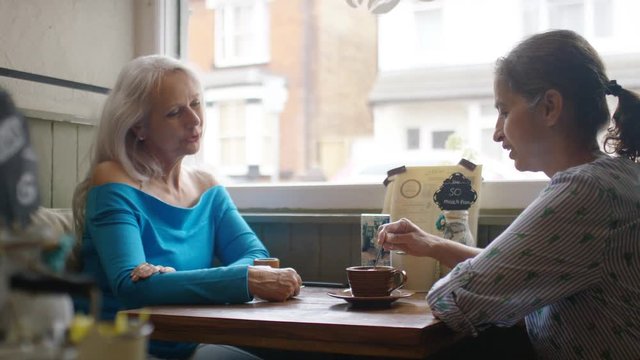 Two older mature ladies in a cafe having a conversation, in slow motion