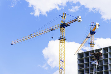 Crane and building under construction against blue sky with clouds