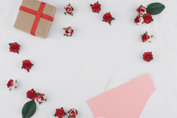 Brown gift box and pink card in white envelop decorate with red rose paper flowers on white fabric with copy space