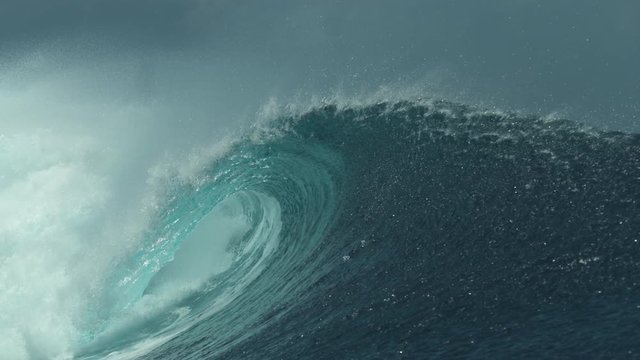 SLOW MOTION, CLOSE UP: Crystal clear ocean water glistens in the bright tropical sunshine while a large tube wave crashes near a remote island in French Polynesia. Picturesque big glassy barrel wave.