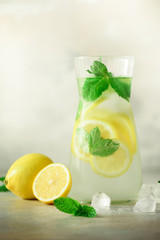 Detox water with mint, lemon on grey background. Banner with copy space, sunlight bokeh. Citrus lemonade. Summer fruit infused water.