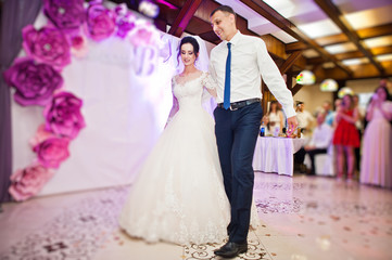 Happy wedding couple performing their first dance in restaurant in front of guests.