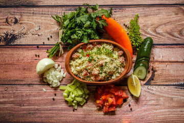 Delicious homemade vegetarian couscous with tomatoes,cucumber,pepper,onion,lemon,parsley and basil on wooden background