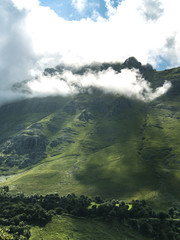 Montaña de verde vegetación con rayos de sol entre nubes y niebla en la cima.