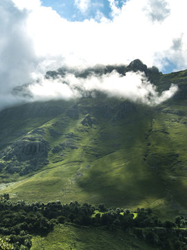 Fototapeta Montaña de verde vegetación con rayos de sol entre nubes y niebla en la cima.