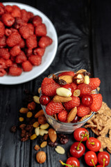 homemade yoghurt with flakes, nuts and berries of raspberries and cherries on dark wooden background