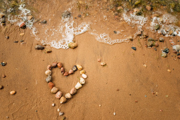 Heart shape from sea stones on a sandy ocean beach, top view, copy space. Love summer vacation background, romance concept