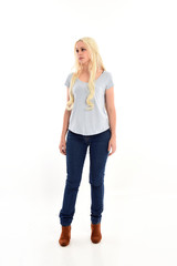 full length portrait of blonde girl wearing blue shirt and jeans, standing pose isolated on white studio background.