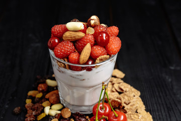 homemade yoghurt with flakes, nuts and berries of raspberries and cherries on dark wooden background