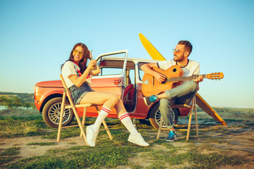 Couple sitting and resting on the beach playing guitar on a summer day near river