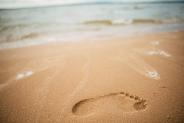 Footprints in the sand at sunset. Beautiful sandy tropical beach with sea waves. Footsteps on the shore.