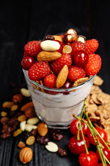 homemade yoghurt with flakes, nuts and berries of raspberries and cherries on dark wooden background, spoon for eating in glass