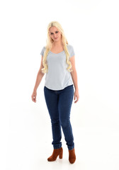 full length portrait of blonde girl wearing blue shirt and jeans, standing pose isolated on white studio background.