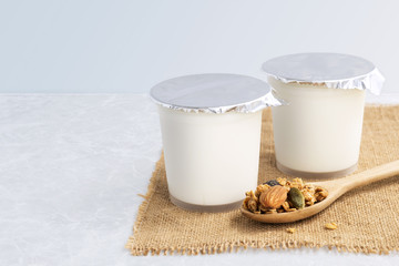 Healthy flavored yogurt in plastic cup with granola and cereal in a wooden spoon on the sackcloth with isolated on gray background. with copy space for text.