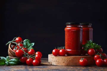 Tomato sauce in a glass jar, tomatoes and herbs on its side.