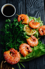 Large grilled BBQ shrimp with sweet chili sauce and lemon, salad.parsley dill celery skewer, dark background, shrimps prawns skewers with herbs