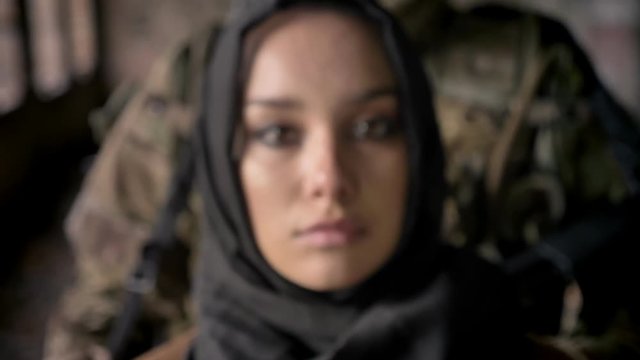 Portrait of young woman in hijab, soldier standing behind her
