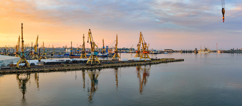 Golden sunset over sea port at summer. Reflections of port facilities and beautiful sky in mirror &ndash; like calm water