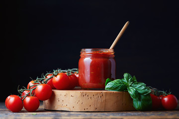 Tomato sauce in a glass jar, tomatoes and herbs on its side.
