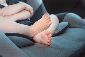 a small child is sitting in a child seat in a car, legs and heels close-up