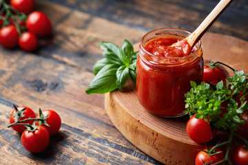 Tomato sauce in a glass jar, tomatoes and herbs on its side. - obrazy, fototapety, plakaty