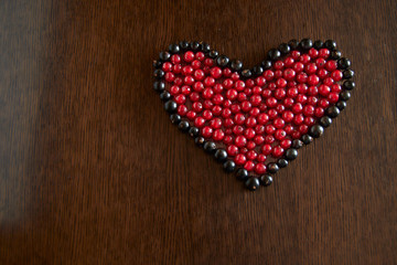The berries of red currant in the frame of black currant berries are laid out in the form of a heart on a wooden dark background.