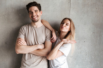 Happy cheerful couple girl and guy in basic clothing smiling at camera, isolated over concrete gray wall indoor in studio
