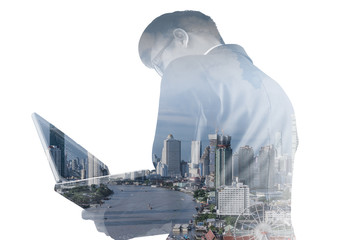 The double exposure image of the business man using a laptop computer during sunrise overlay with cityscape image. The concept of modern life, business, city life and internet of things.