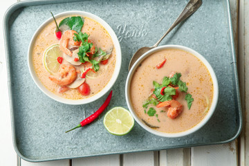 Traditional thai soup tom yum with shrimps and mushrooms, served with fresh lime slices on metallic tray