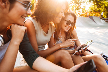 Three friends woman using mobile phones listening music with earphones.