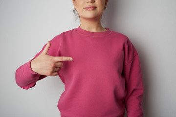 Young hipster girl wearing pink hoody with space for your logo or design. Mock-up of pink hoody on gray empty wall in the background