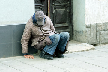 poor homeless man sitting near the wall of the building