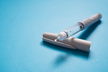 Insulin pen with insulin drop at needle tip on light blue background. Medical devices is used to...