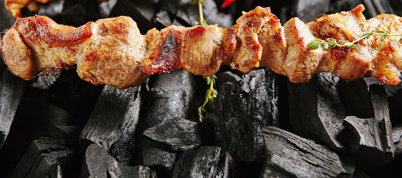 Hot Grilled Pork Kebab or Barbecue Shashlik on Charcoal Background with Herbs and Spices