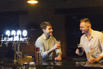 Two happy young men talking and drinking beer at bar