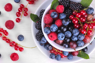 Various fresh berries close-up including blueberries, raspberries, blackberries and currants in a white cup on a white wooden background. Top view