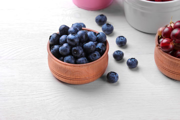 Fresh, large blueberry in a wooden bowl close-up next to other berries on a white wooden background. top view